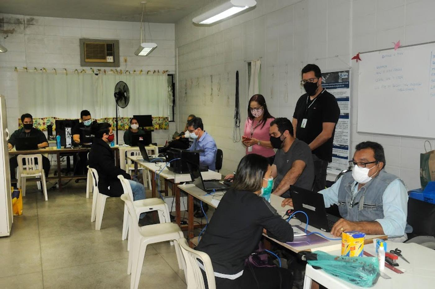 pessoas estão sentadas à mesa. De um lado, são atendentes. De outro, o público do centro de emprego. #paratodosverem 