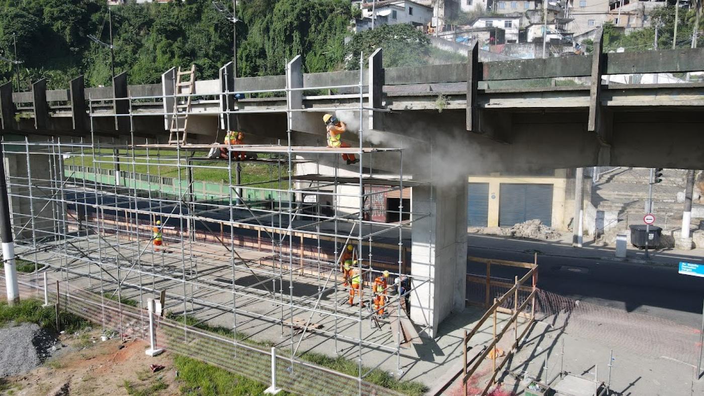 andaime na lateral de elevado, com homens trabalhando junto à estrutura. #paratodosverem