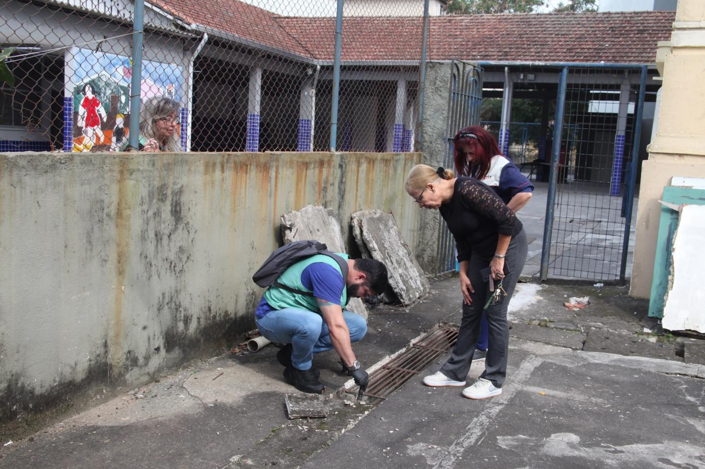 agente de saúde examina grelha em solo de escola. #paratodosverem 