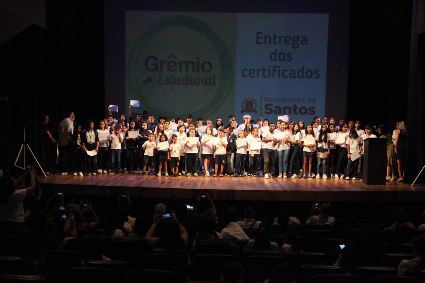 crianças seguram diploma em palco. #paratodosverem