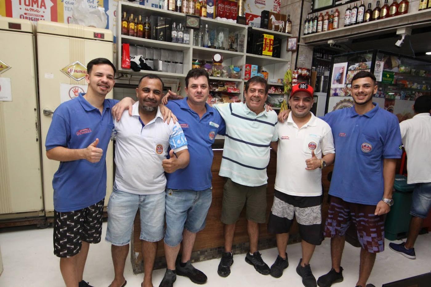 Homens abraçados em frente a balcão de restaurante. #paratodosverem
