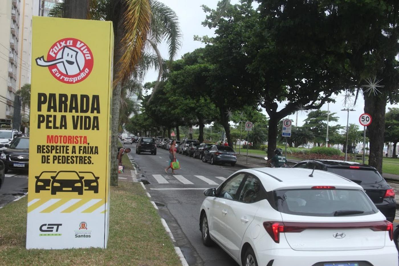 cubo em torno de posto onde se lê parada pela vida. motorismta, respeite a faixa de pedestre. Ao lado, a via com carros parados diante de uma faixa. #paratodosverem 