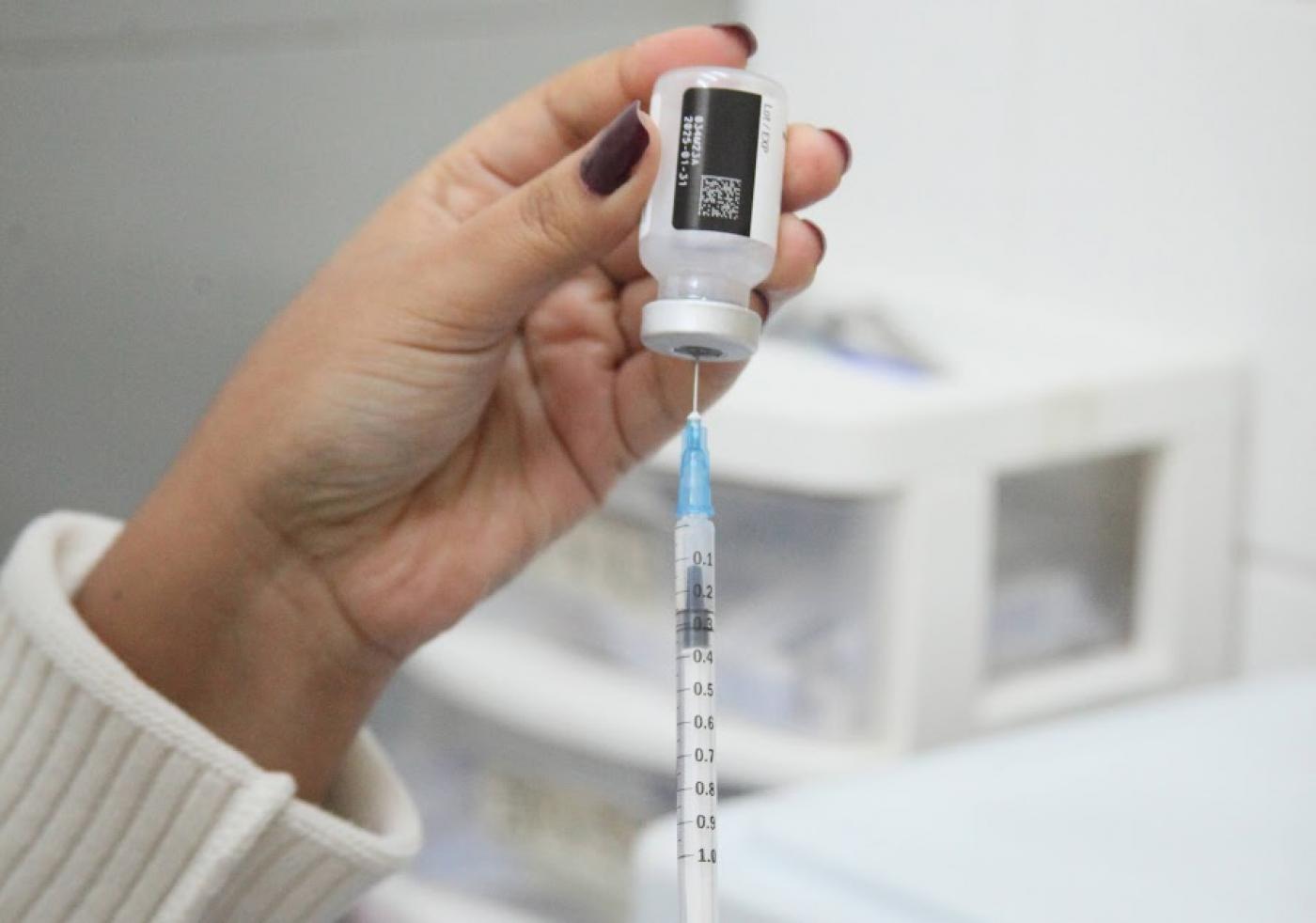 mão segura seringa e frasco de vacina. #paratodosverem 