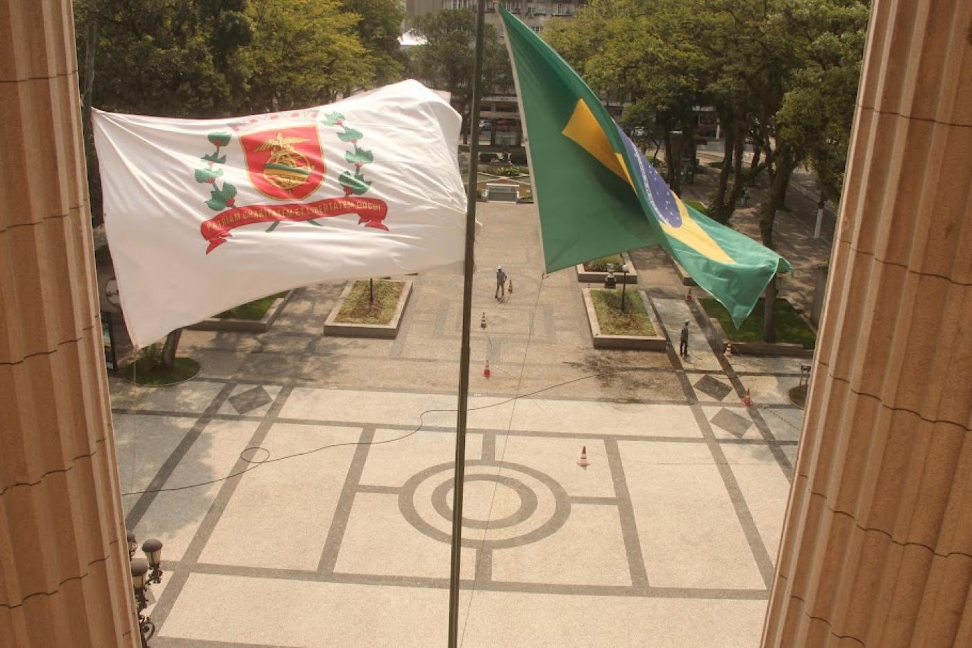 vista do piso da praça mauá da sacada da prefeitura. Em primeiro plano, as bandeiras de Santos e do Brasil tremulando e o piso ao fundo. #paratodosverem