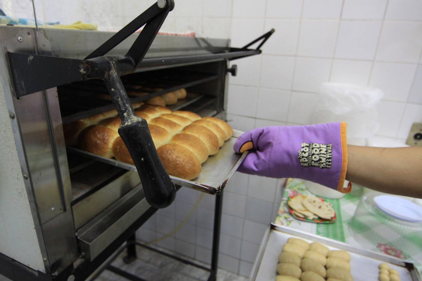 mão com luva retira bandeja com pães de dentro de forno. #paratodosverem 