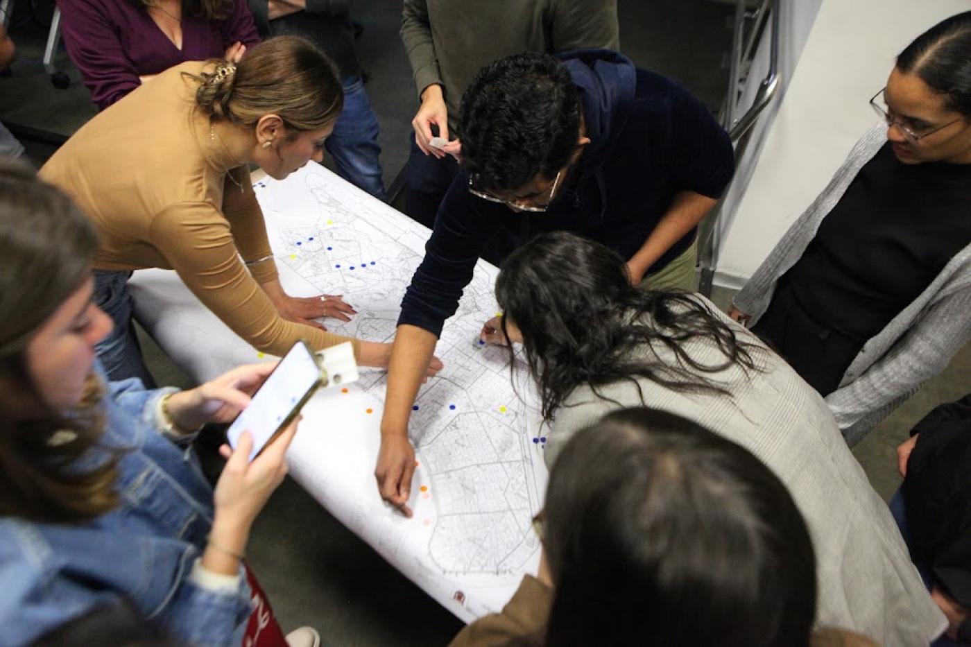 pessoas observam mapa sobre uma mesa. #paratodosverem