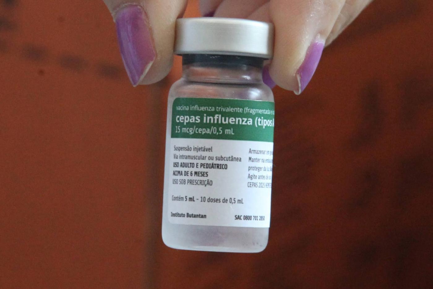 mão segura frasco de vacina contra a gripe. #paratodosverem 