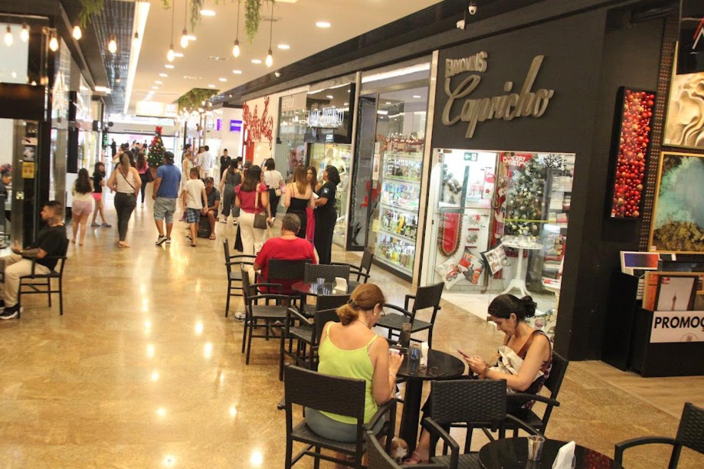 corredor de shopping com pessoas snetadas em mesas de cafezinho e circulando. #paratodosverem 