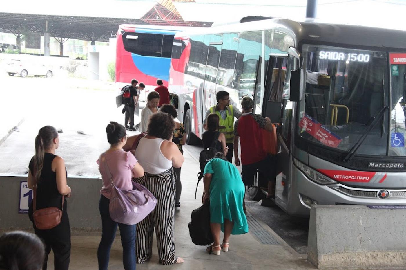 pessoas em fila para entrar em ônibus parado em baia de terminal rodoviário. #paratodosverem 