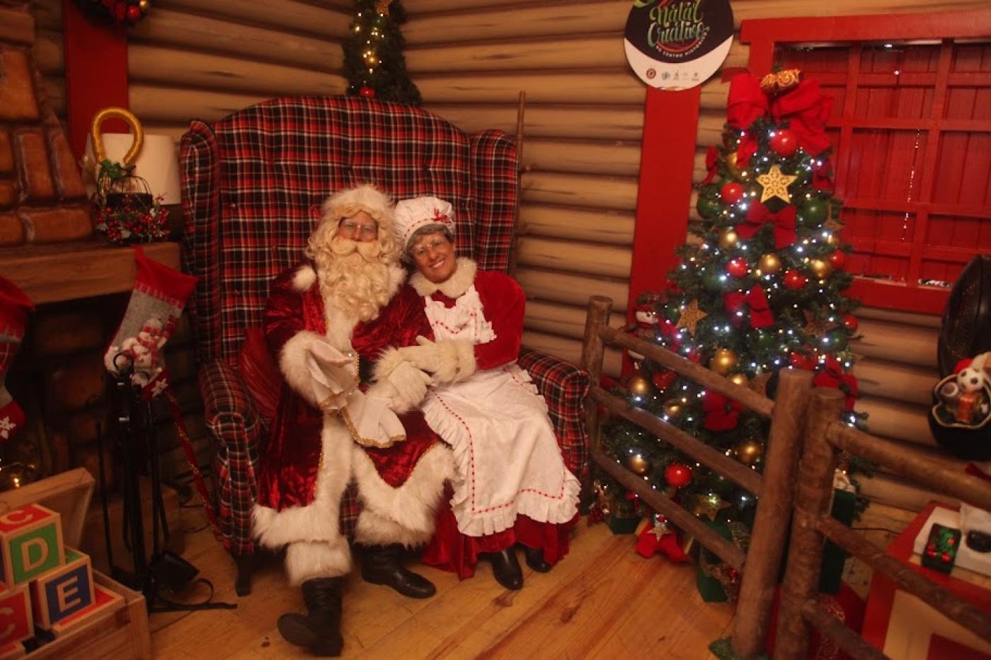 papai e mamãe noel estão sentados juntos na casinha do papai noel. #paratodosverem 