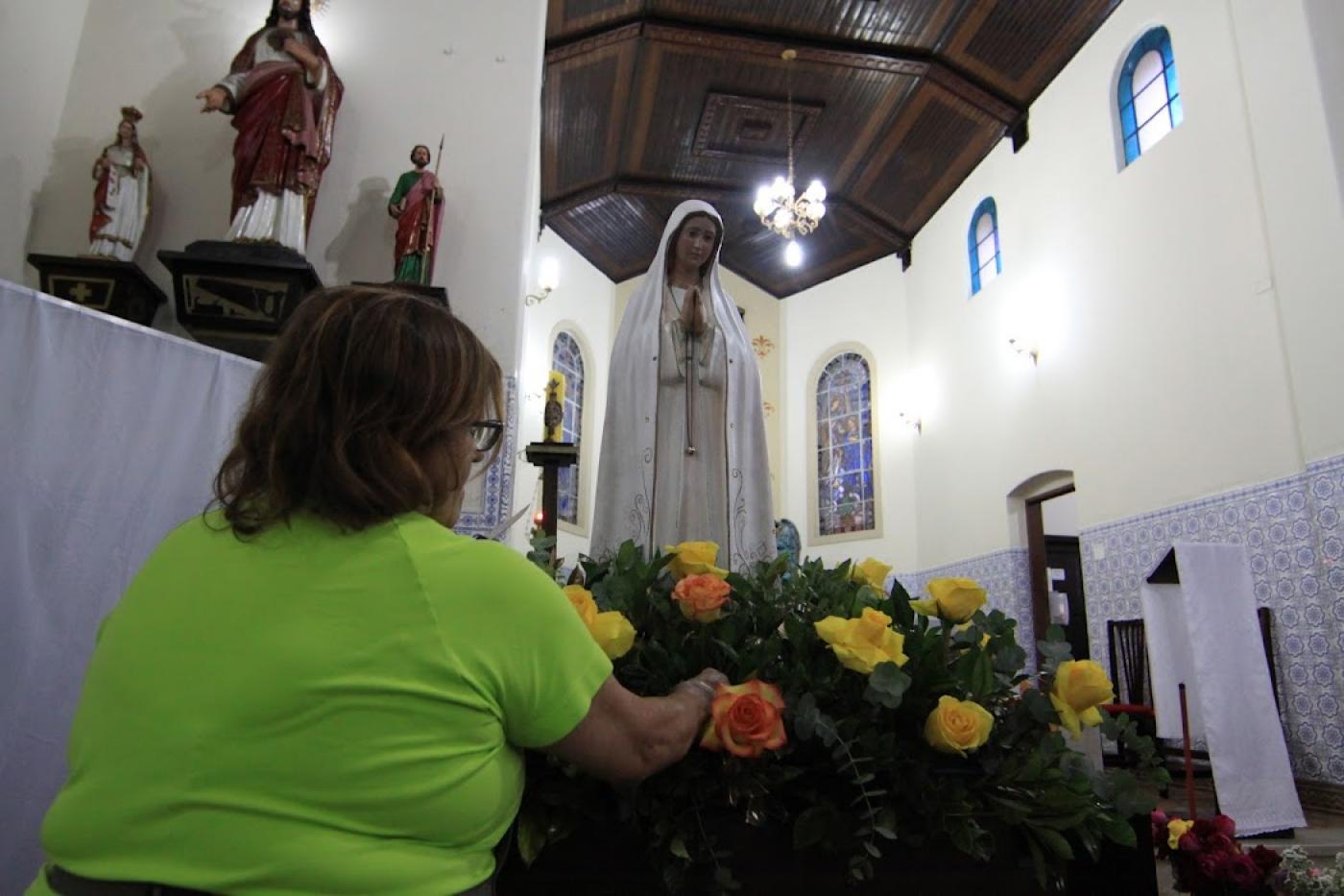 mulher arruma arranjo de flores na frente da santa #paratodosverem