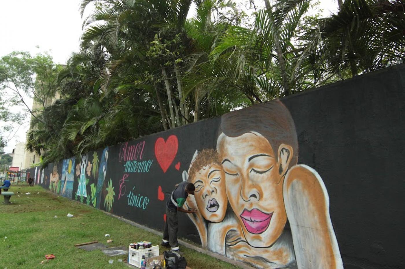 homem está grafitando muro. por trás, muitas árvores. #paratodosverem