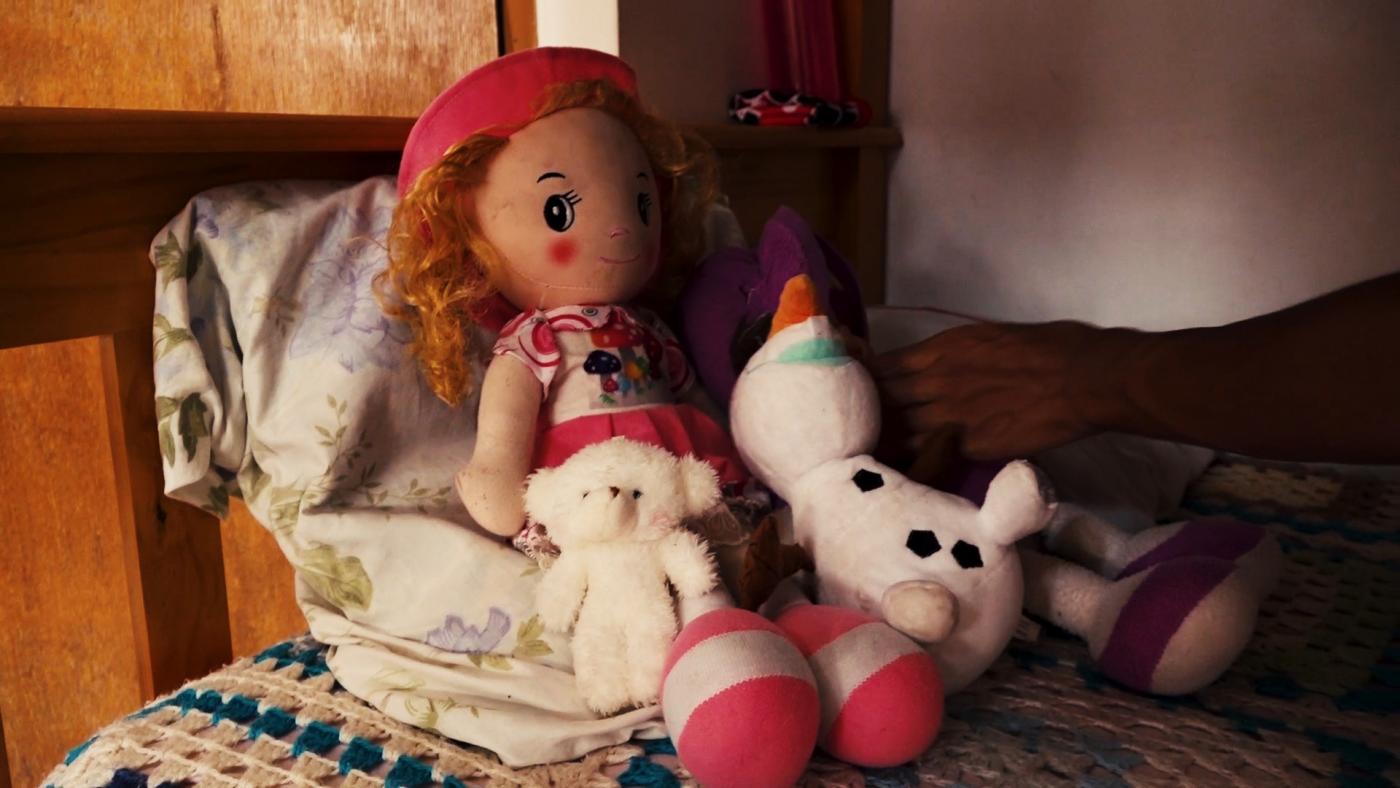 boneca e bichos de pelúcia sobre uma cama. #paratodosverem