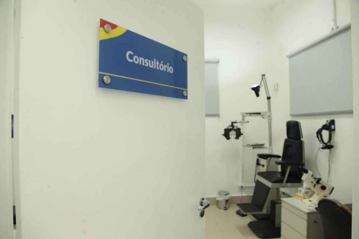 Porta do consultório entreaberta com cadeira oftalmológica ao fundo. #pracegover