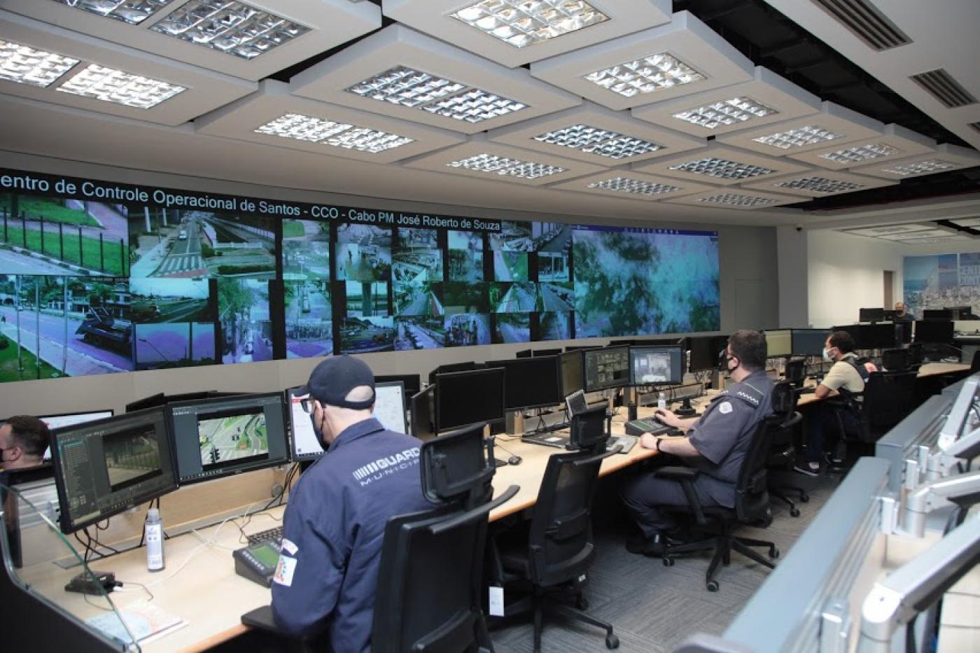 vista geral do Centro de Controle Operacional com homens trabalhando diante de um grande telão. #paratodosverem