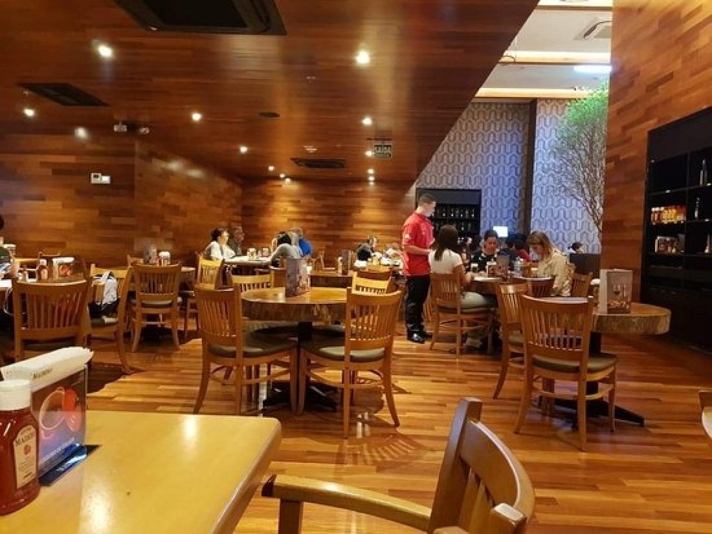 salão de restaurante com mesas e algumas pessoas sentadas. #paratodosverem