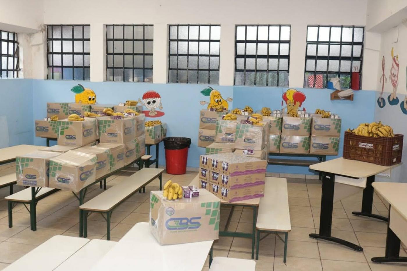Caixas com alimentos estão sobre mesas escolas. #Paratodosverem