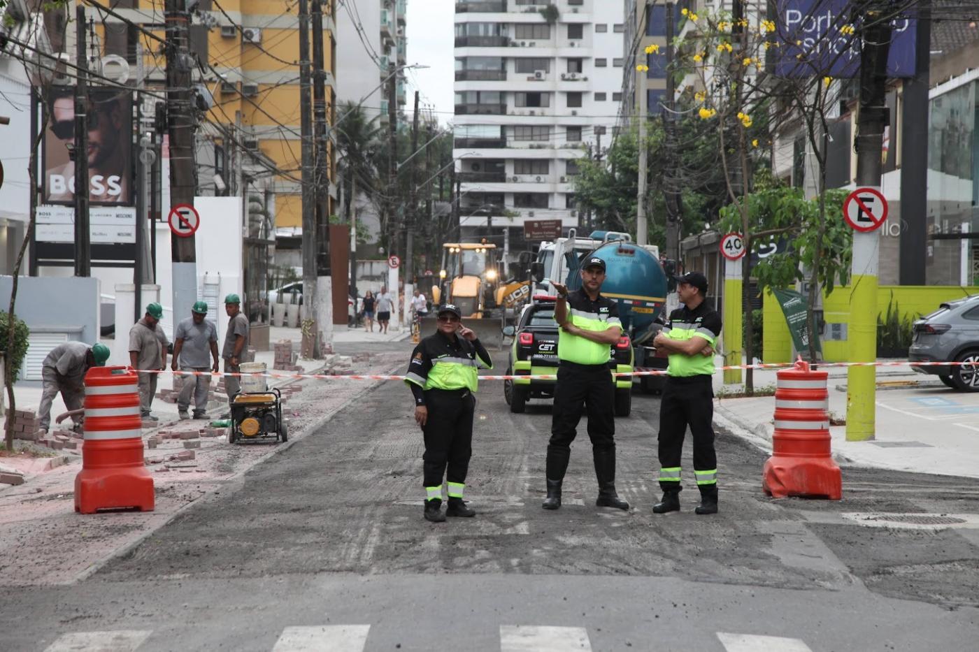 agentes de trânsito estão parados em rua em obras ao lado de cones. #paratodosverem