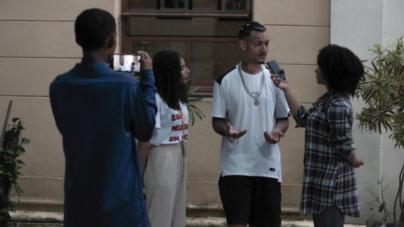 jovem está em pé sendo entrevistado por estudantes. #paratodosverem 