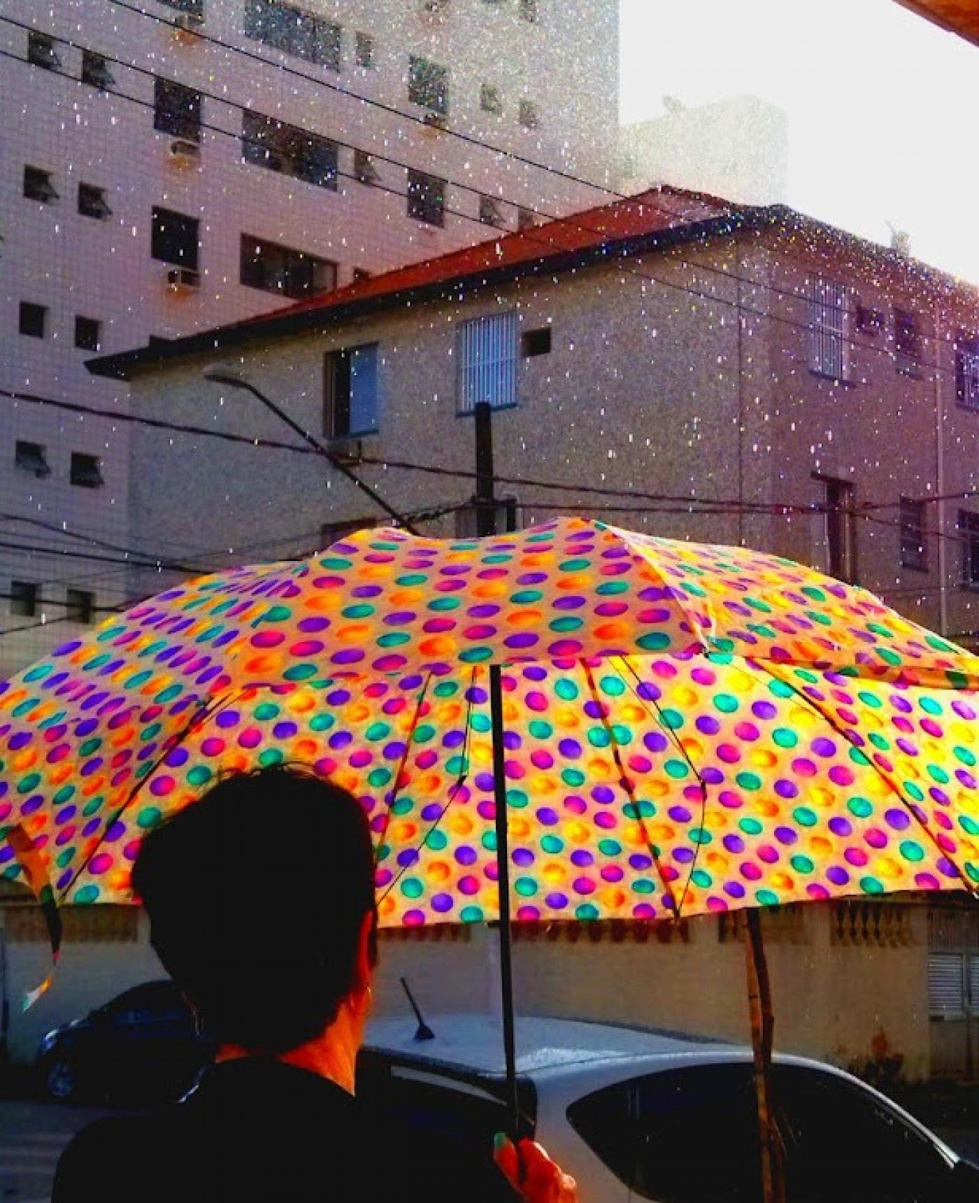 uma pessoa de costas para a foto está segurando um guarda chuva aberto na rua. #paratodosverem