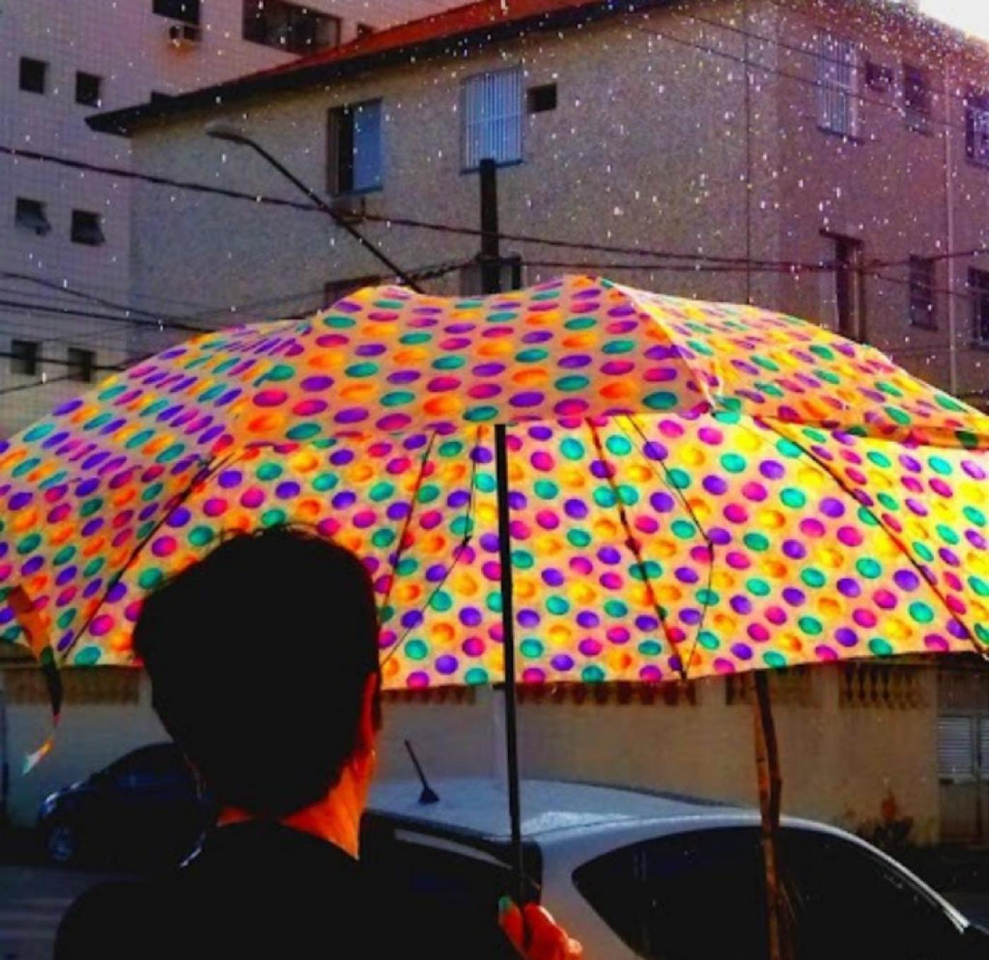 pessoa de costas está segurando guarda chuva ultra colorido em meio ao cenário cinzento e chuvoso. #pratodosverem