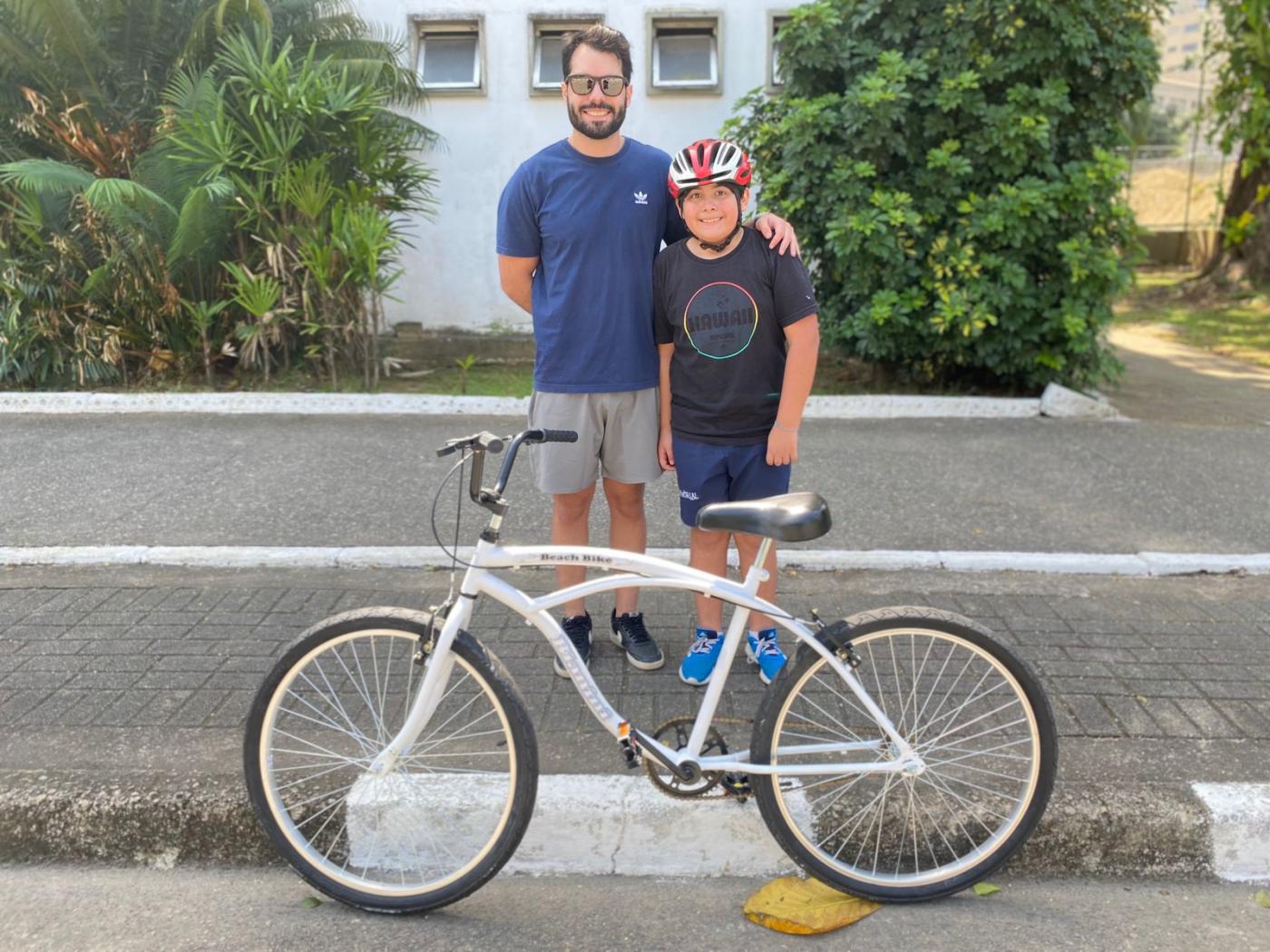Pai e filho posam na frente da bicicleta. #Paratodosverem