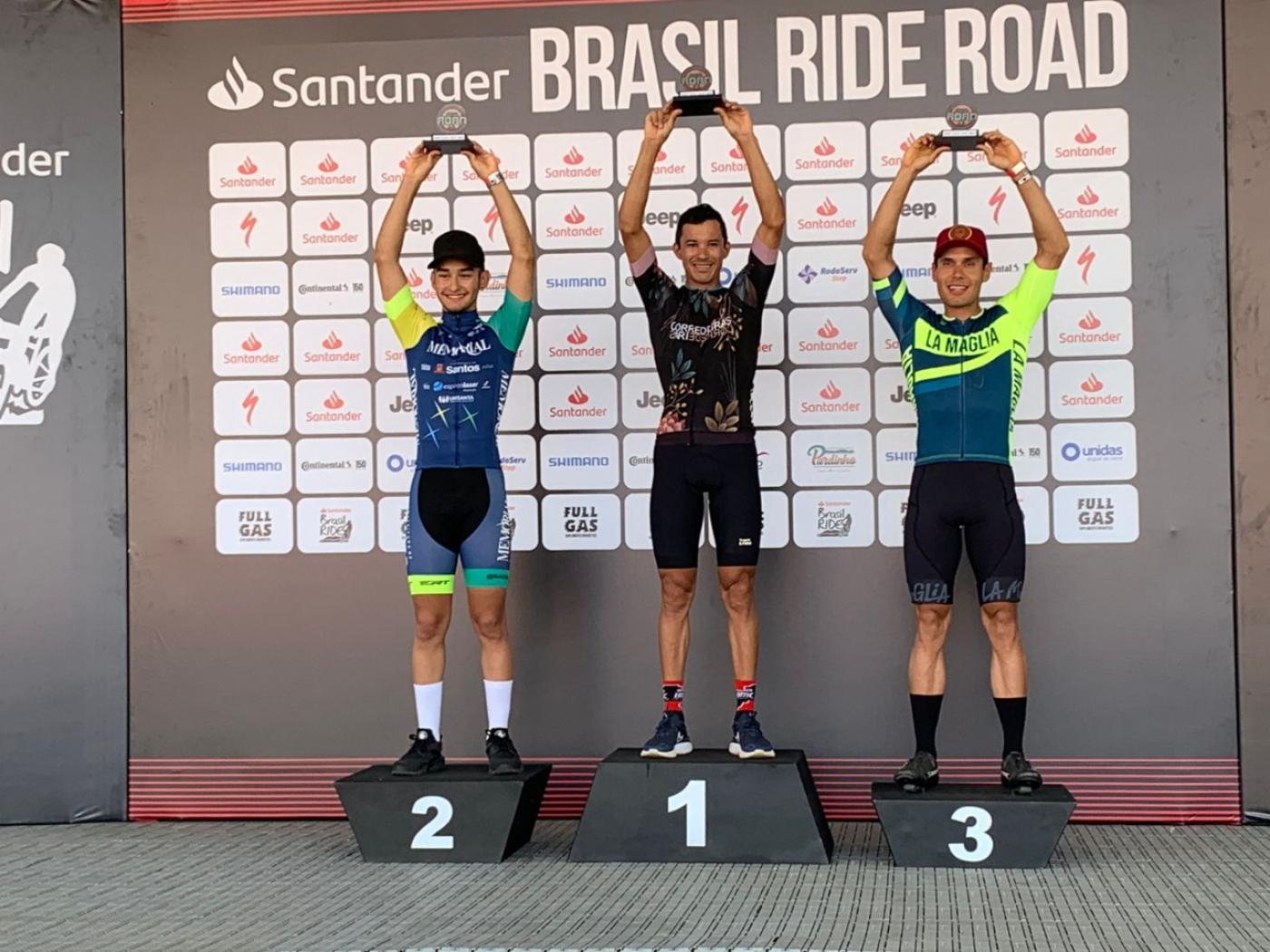 Ciclistas levantam troféus no pódio #paratodosverem