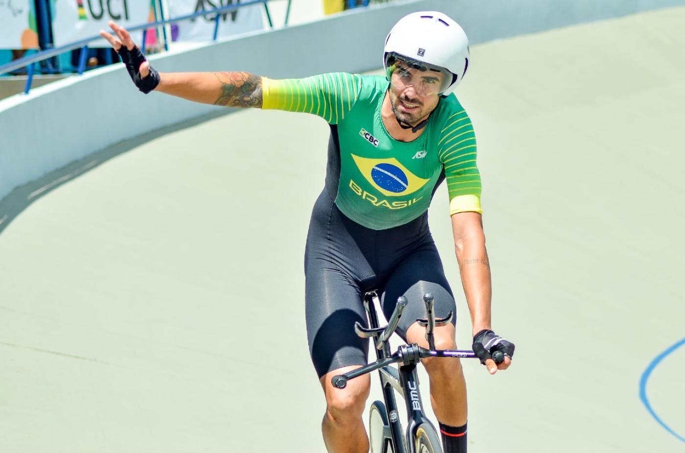 atleta sobre bicicleta com capacete , com braço direito esticado #paratodosverem