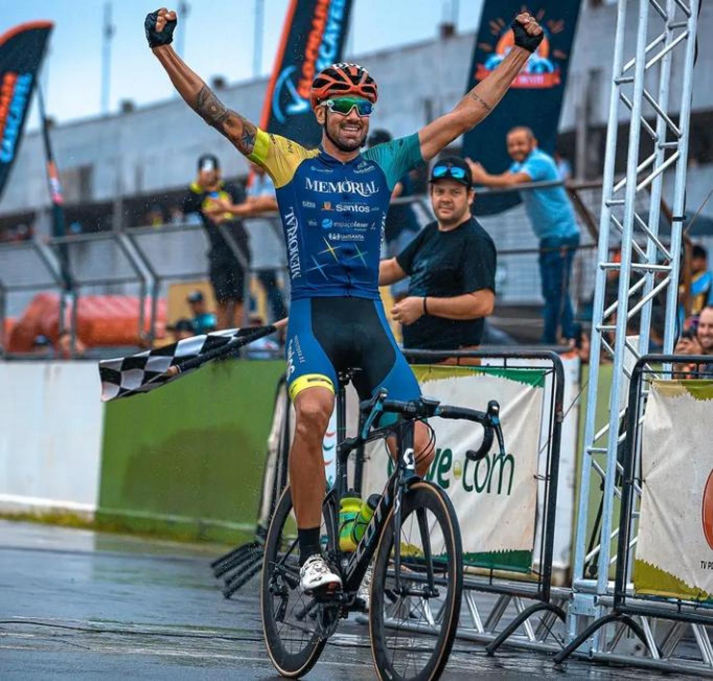 Atleta, sobre a bicicleta, levanta os braços na chegada. #pratodosverem