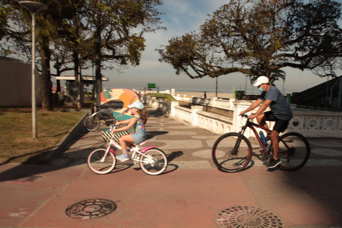 Pai e filha andando de bicicleta na ciclovia da praia. #paratodosverem