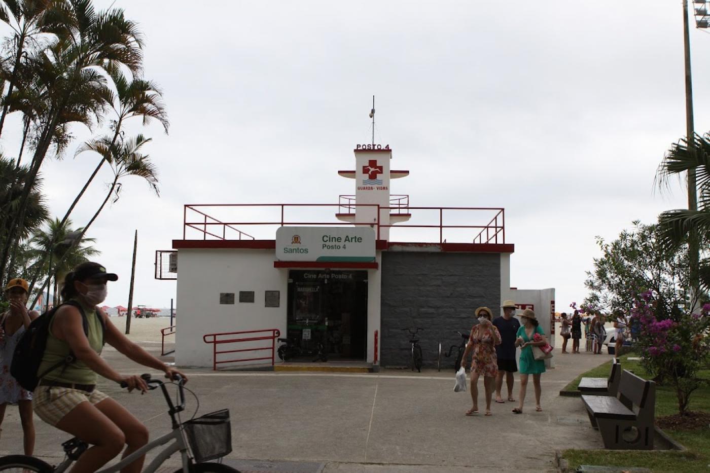 Fachada do Cine Arte Posto 4 na orla com pessoas passando em volta e ciclista em primeiro plano. #pratodosverem