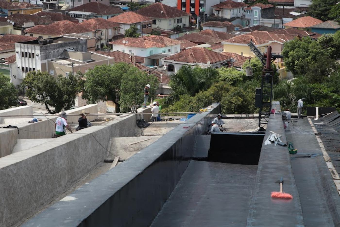 cobertura do teatro em obras, com homens trabalhando ao fundo e vista de prédios da cidade abaixo. #paratodosverem