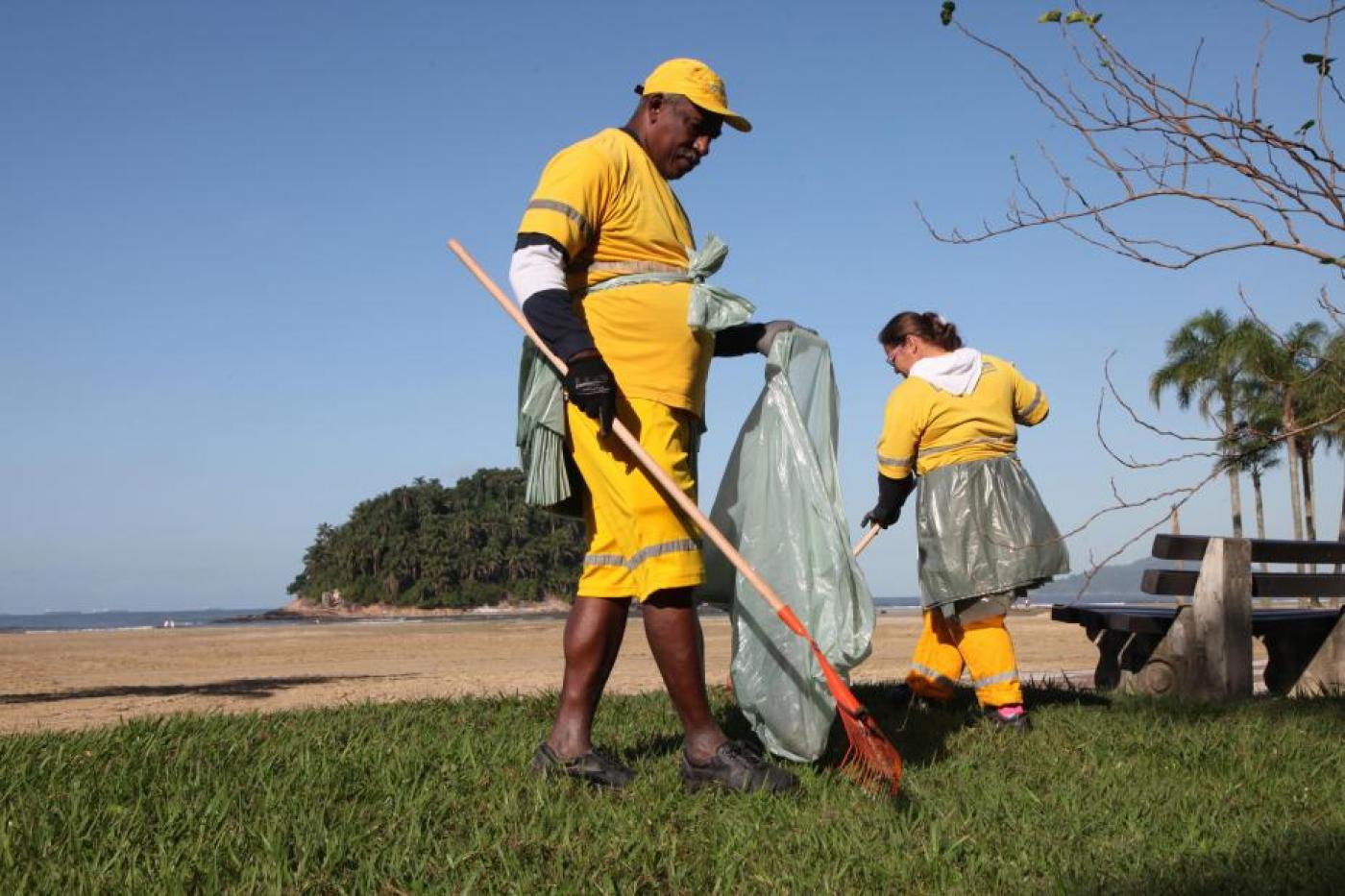 homem e mulher uniformizados removem folhas de jardim da orla. #paratodosverem