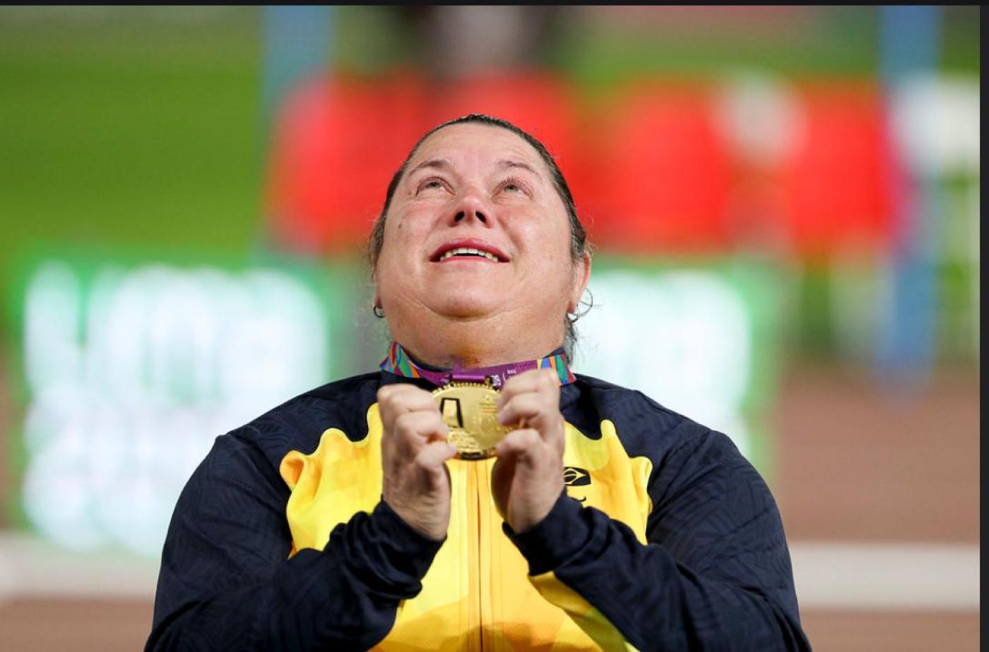 Beth Gomes segura medalha com as duas mãos à frente do peito. Ele olha para o alto. #Pracegover