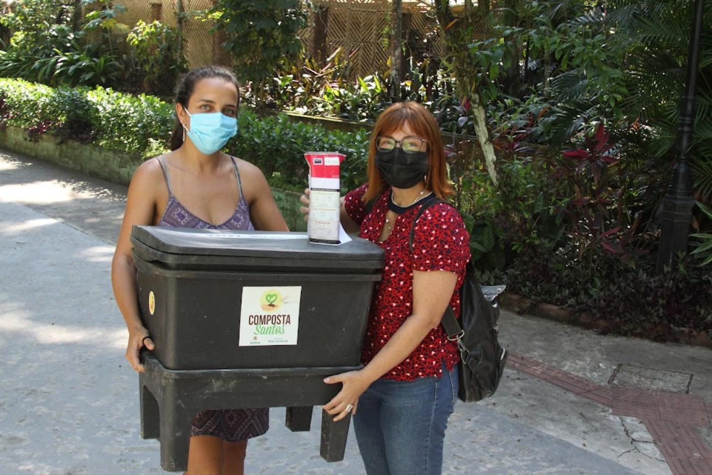 duas mulheres seguram composteiras juntas. Elas posam para a foto. #paratodosverem