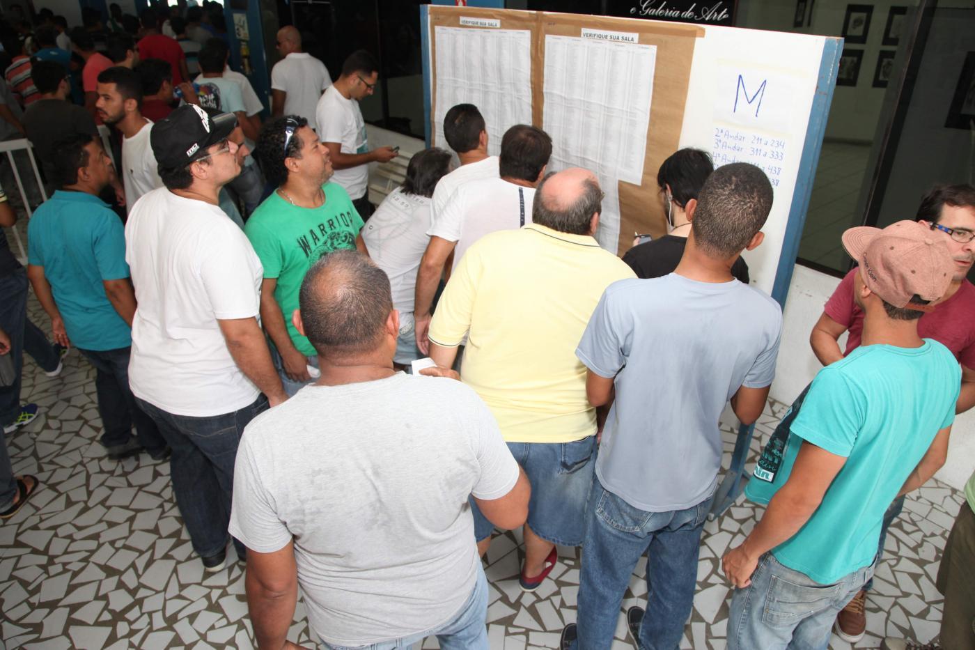 candidatos olham folhas em painel de madeira #paratodosverem