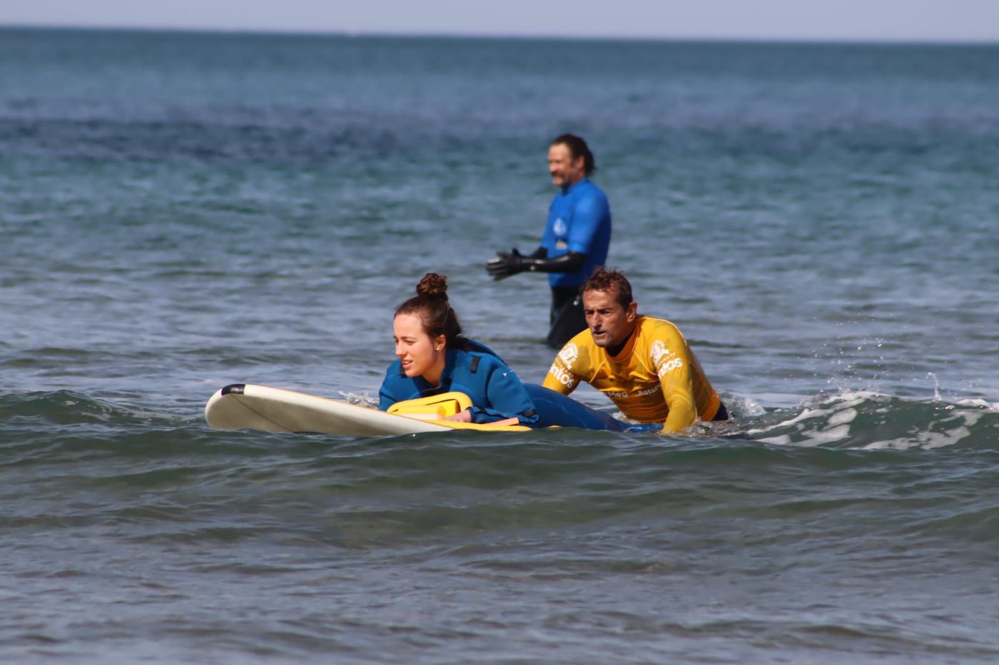 uma pessoa em uma prancha, atrás dela outra a ajuda no mar #paratodosverem