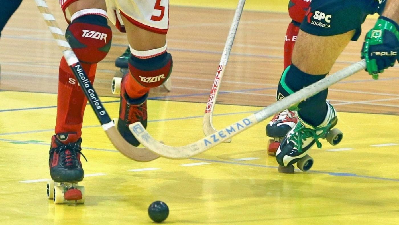 close de disputa de bola entre dois jogados de hóquei sobre patins. Um taco de cada lado é direcionado à bola. #paratodosverem