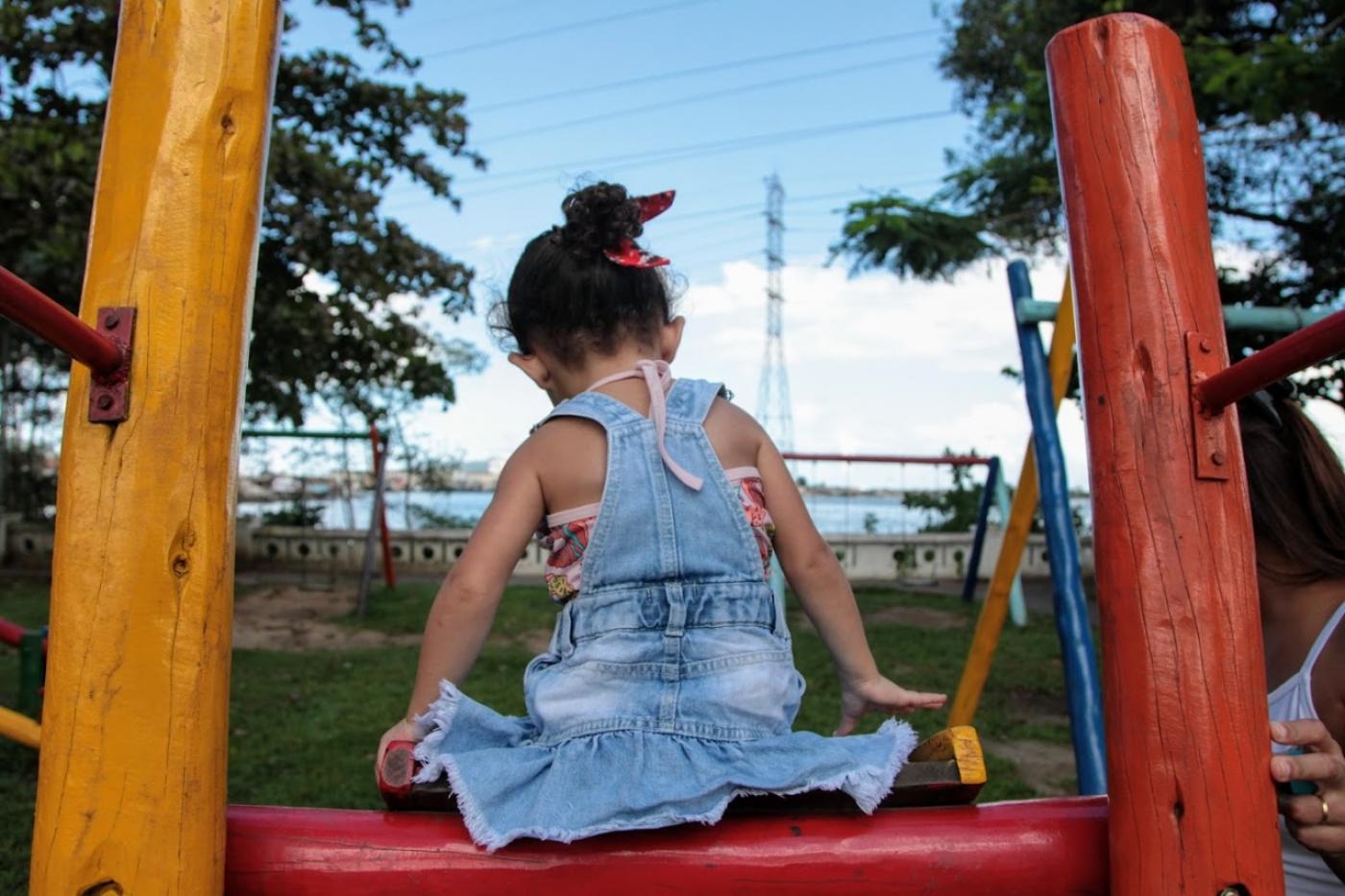 criança de costas para a foto sentada no topo de escorregador. #paratodosverem