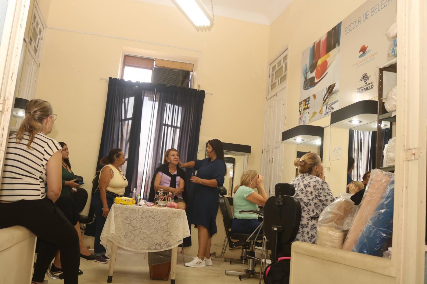 mulheres reunidas com mesa ao centro com produtos de maquiagem. #paratodosverem