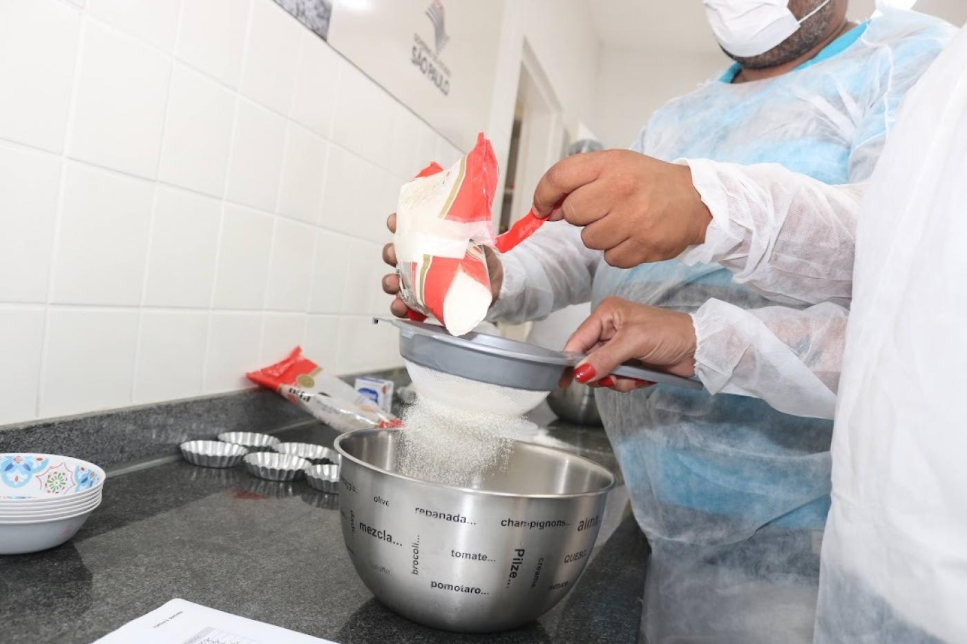 foto em close de mãos coando farinha em pote de alumínio para preparar alimento. #paratodosverem