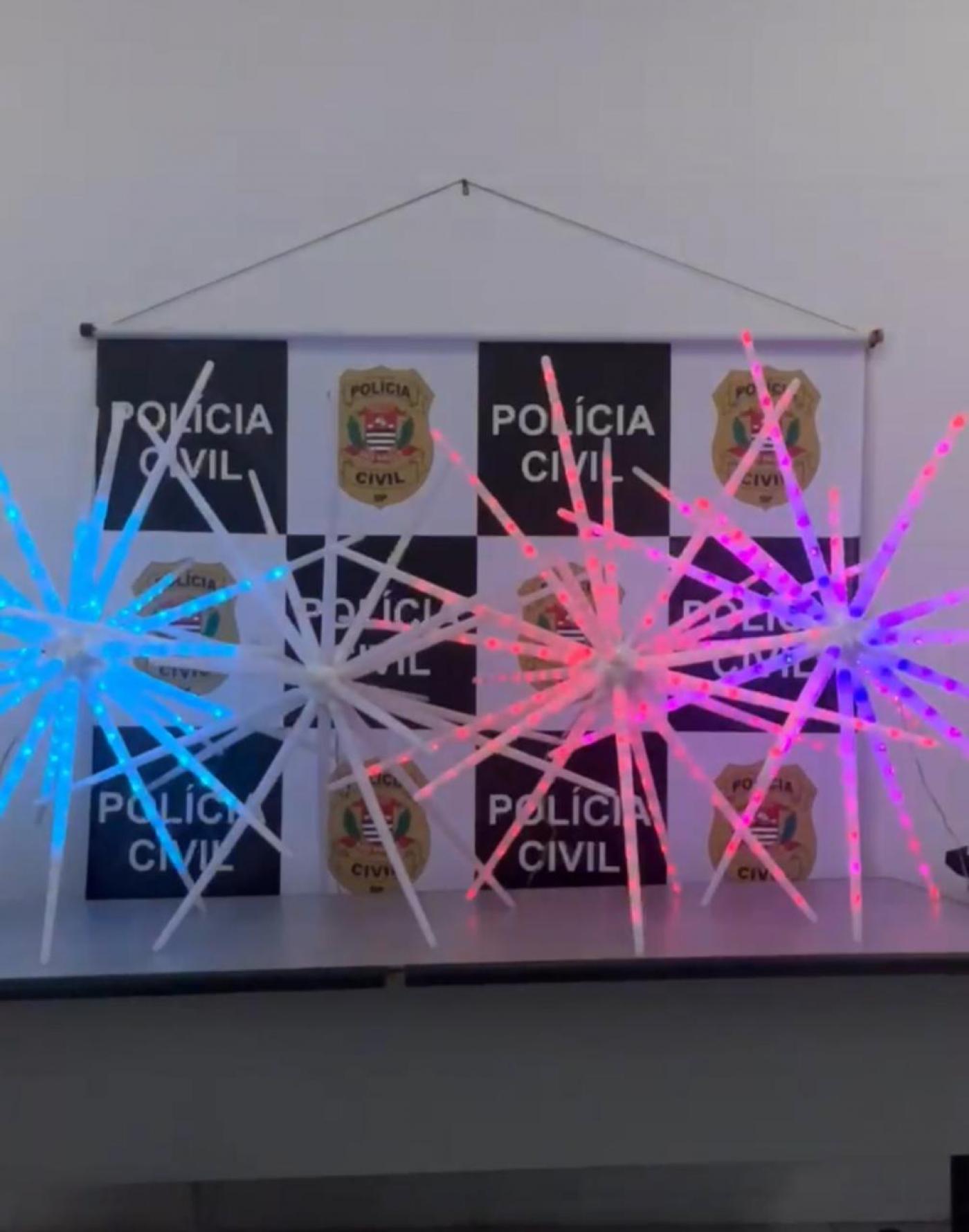 luz de natal tipo sputinik piscando sobre uma pesa com banner da polícia civil ao fundo. #paratodosverem 