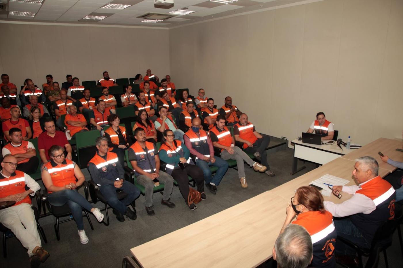 Representantes dos órgãos de Defesa Civil sentados durante treinamento em auditório. #paratodosverem