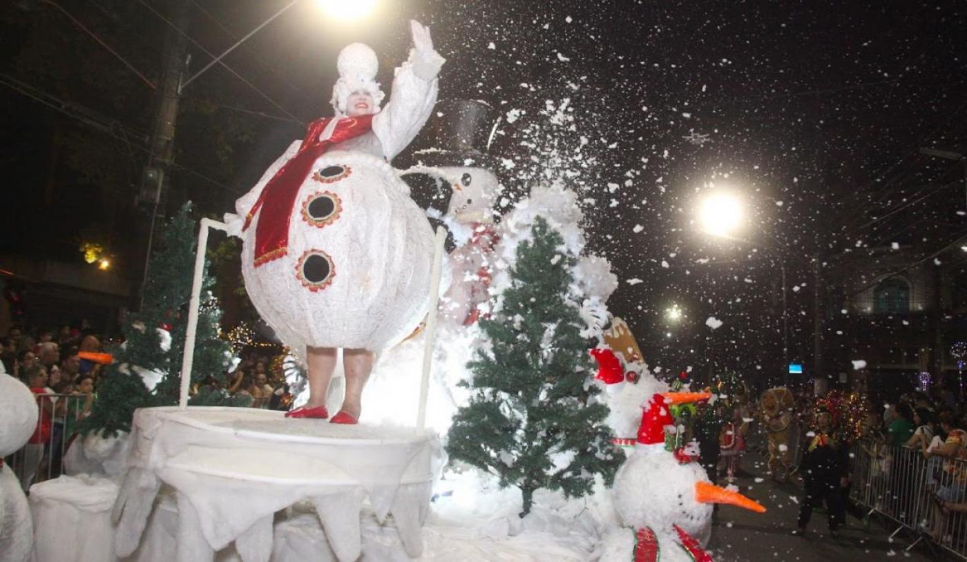 carro alegórico com personagem de boneco de neve. Há 'neve' flutuando no ambiente. #paratodosverem 