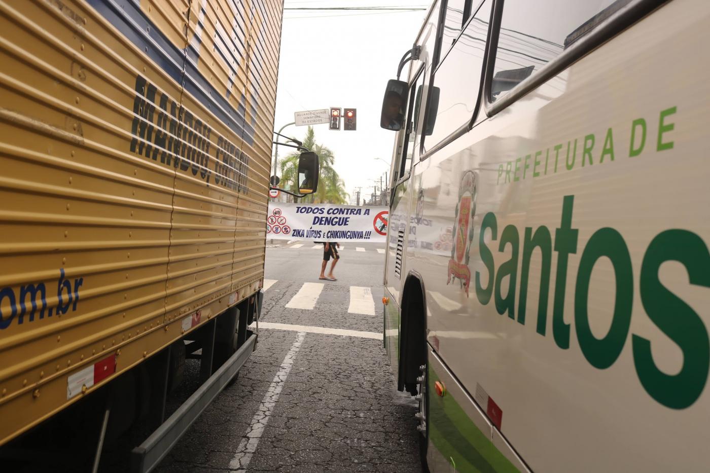 faixa contra o aedes ao fundo, vista entre caminhão e ônibus. #paratodosverem