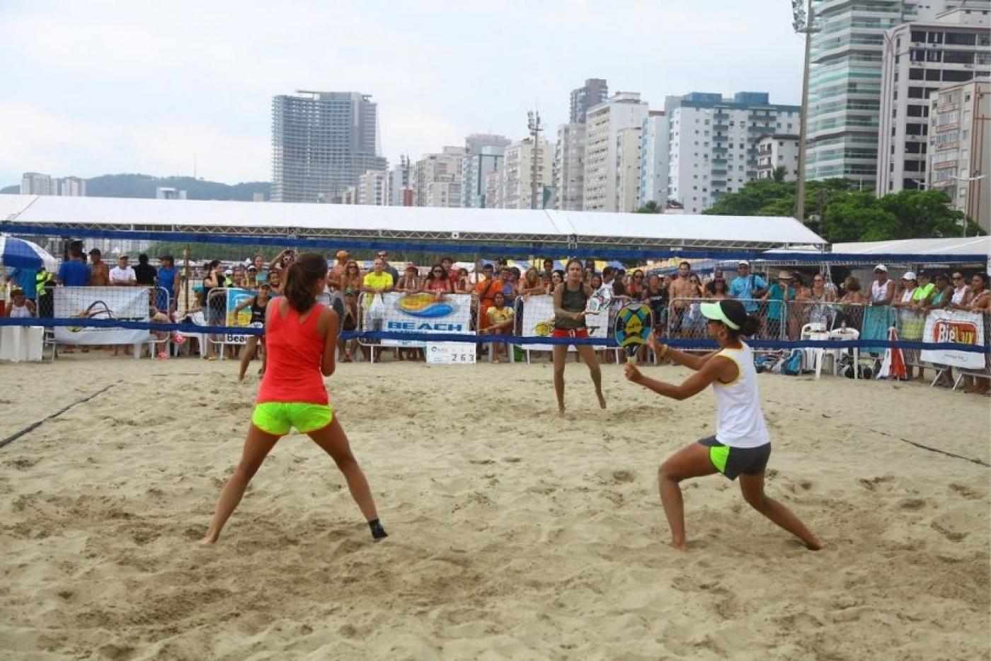 duas pessoas de costas , de frente para uma rede de esportes, em uma praia #paratodosverem