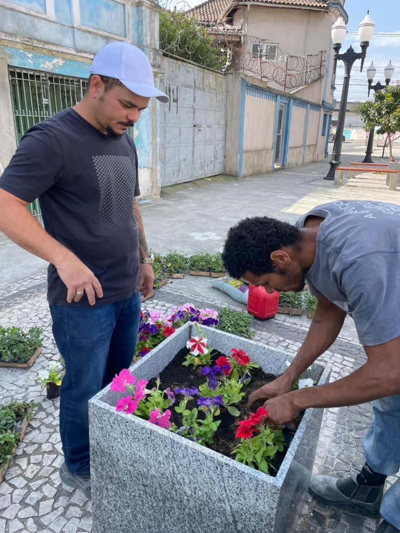 dois homens ajeitam floreira em rua. #paratodosverem