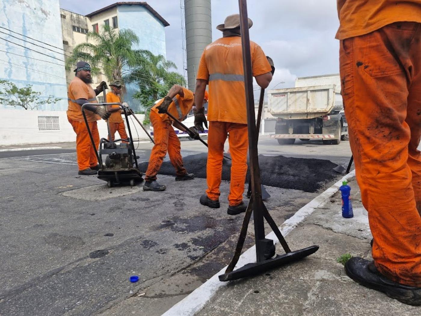 homens cobrem trecho de rua com asfalto. #paratodosverem 