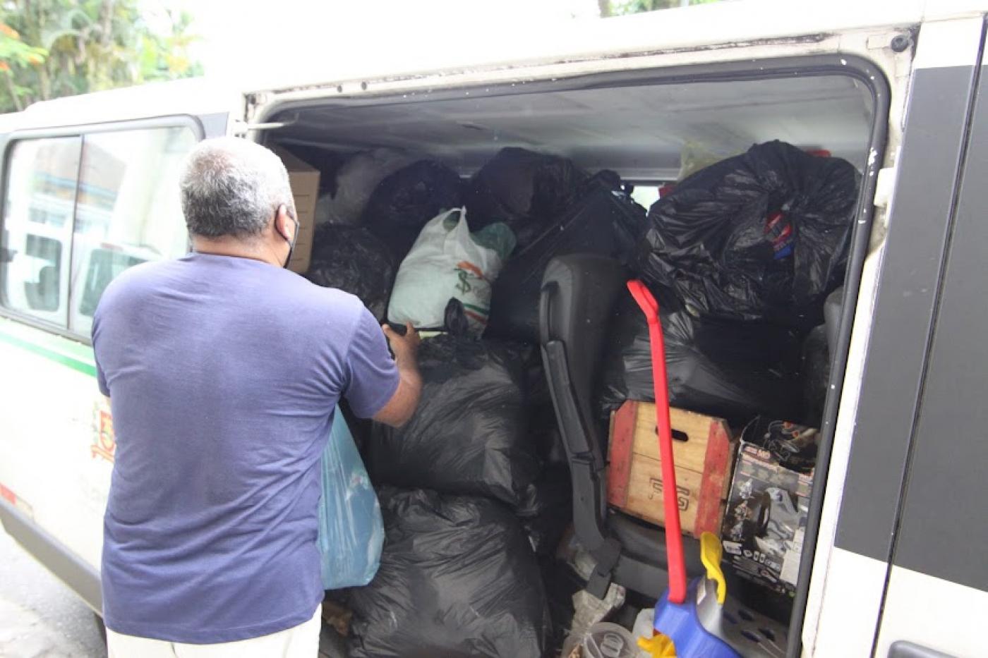 homem está enchendo van com sacos cheios de roupas. O veículo está lotado. #paratodosverem