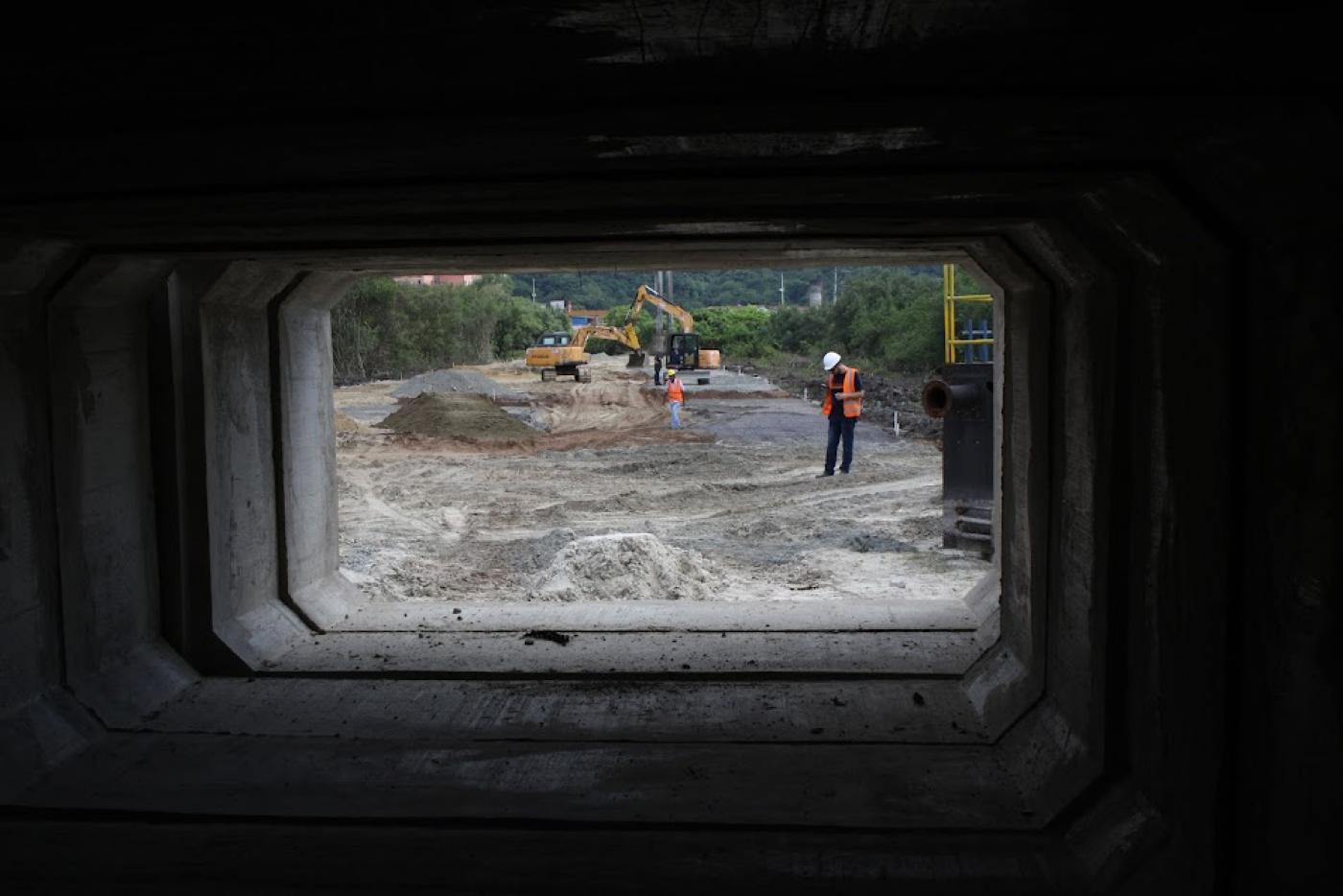 fotógrafo se posicionou na entrada de aduela para fazer dela uma moldura e mostrar a sua proporção em relaão ao homem e máquinas que estão no fundo. #paratodosverem